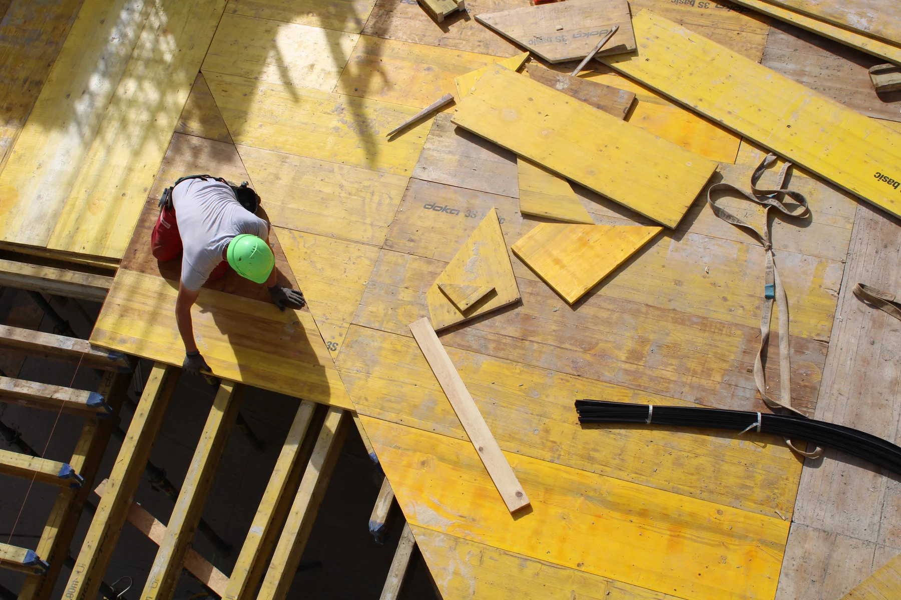 Carpenter placing plywood panels over timber beams to assemble a concrete slab formwork deck
